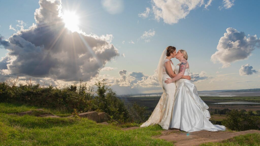 A bride and groom embracing on a grassy hill.