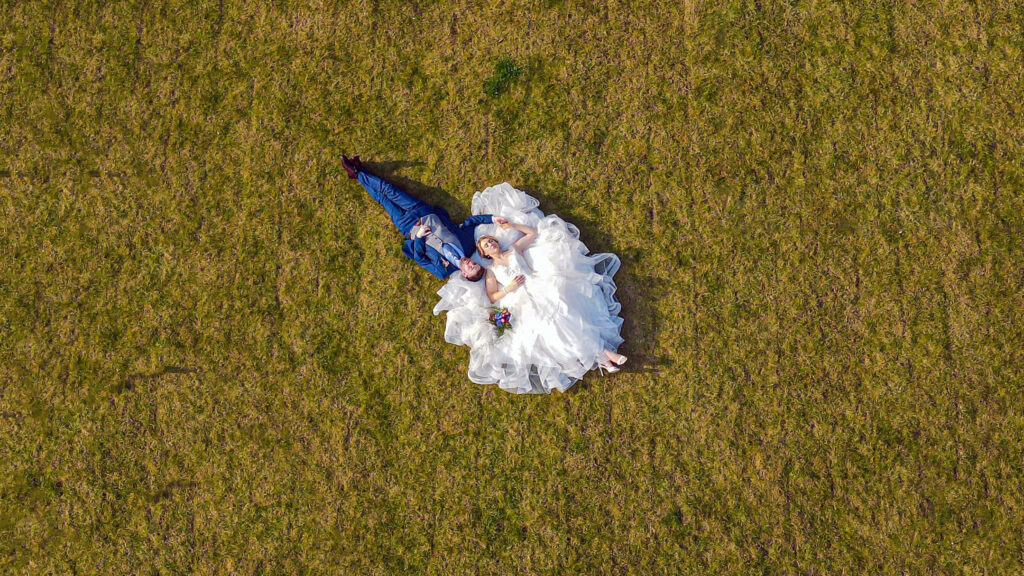 An aerial view of a bride and groom laying in a field.