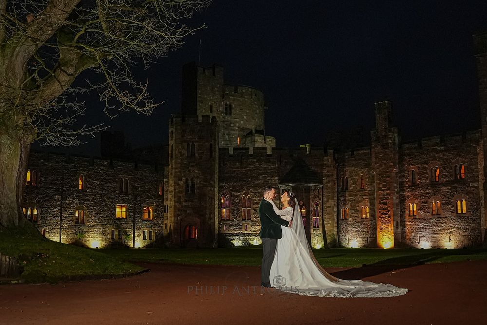 A bride and groom standing in front of a castle at night.