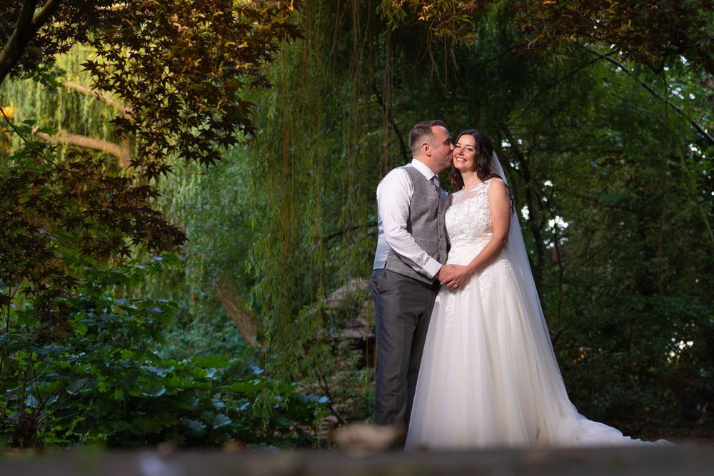 A bride and groom posing in front of a willow tree.