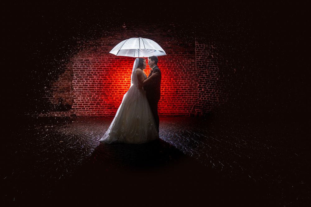 A bride and groom standing under an umbrella in a dark room.
