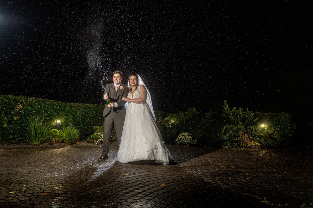 A bride and groom standing under a sprinkler at night.