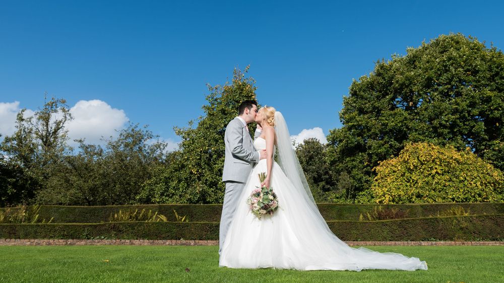A bride and groom kissing on a grassy field.