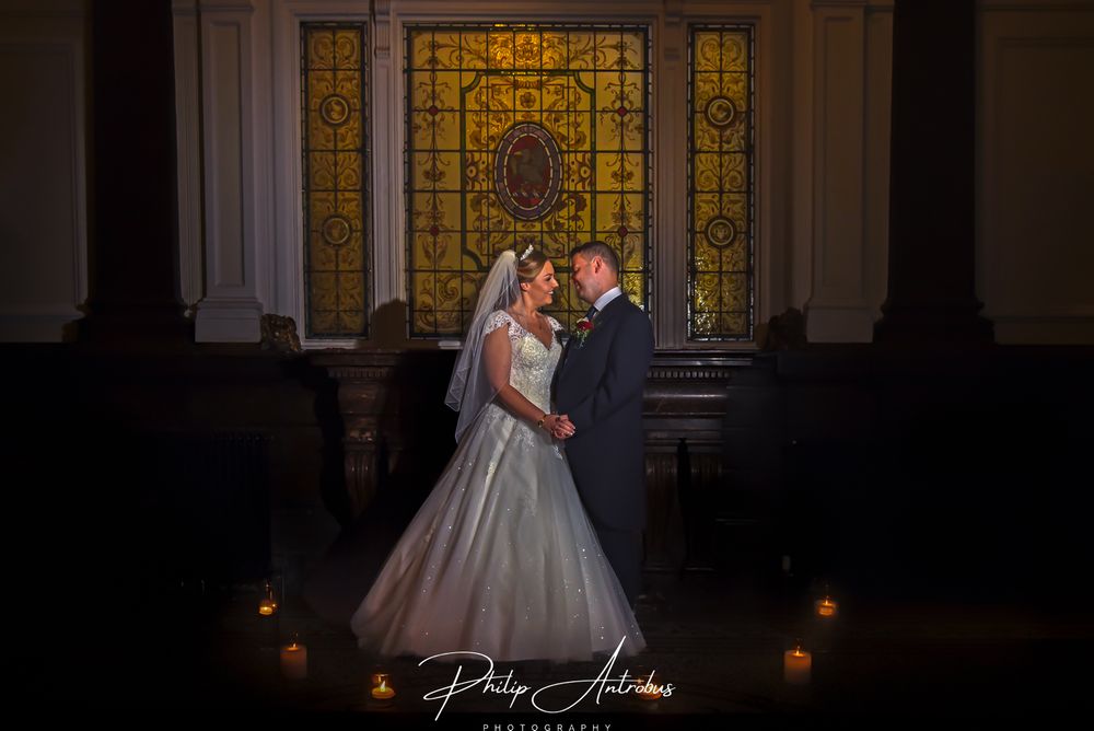 A bride and groom standing in front of a stained glass window.