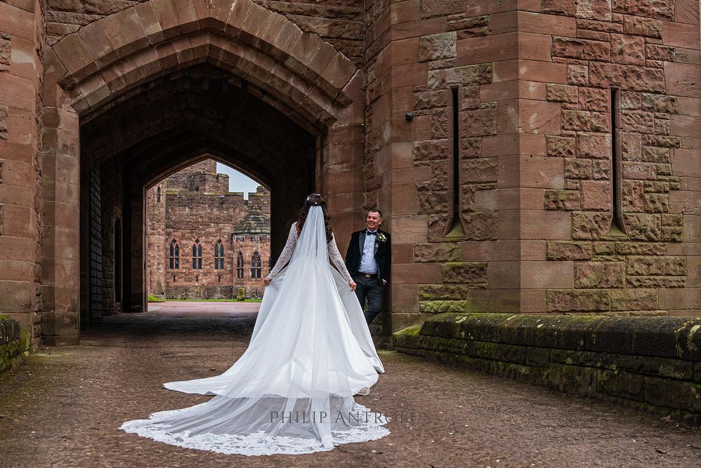 A bride and groom walking through an archway in a castle.