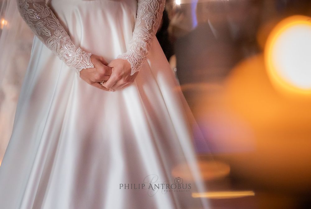 A bride in a white wedding dress holding her hands.