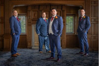 Four groomsmen posing in elegant interior setting.