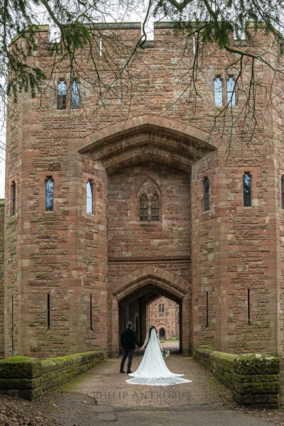 Couple walking towards historic castle entrance in wedding attire.