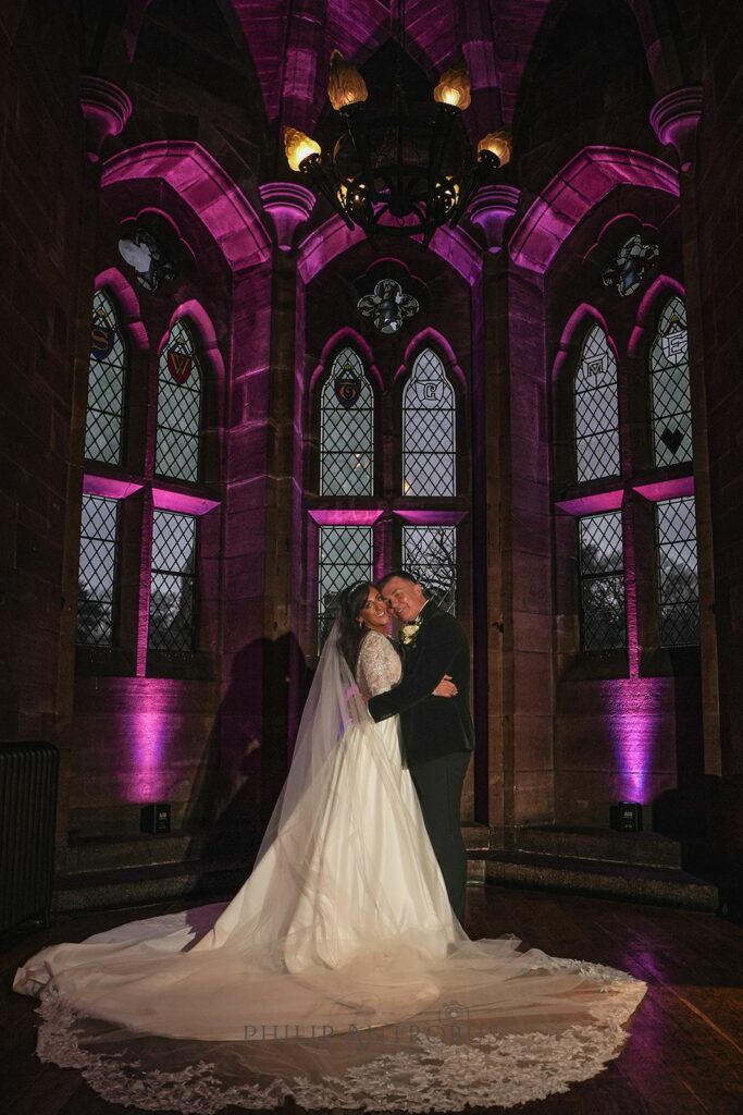 Couple embracing in historic chapel with purple lighting.