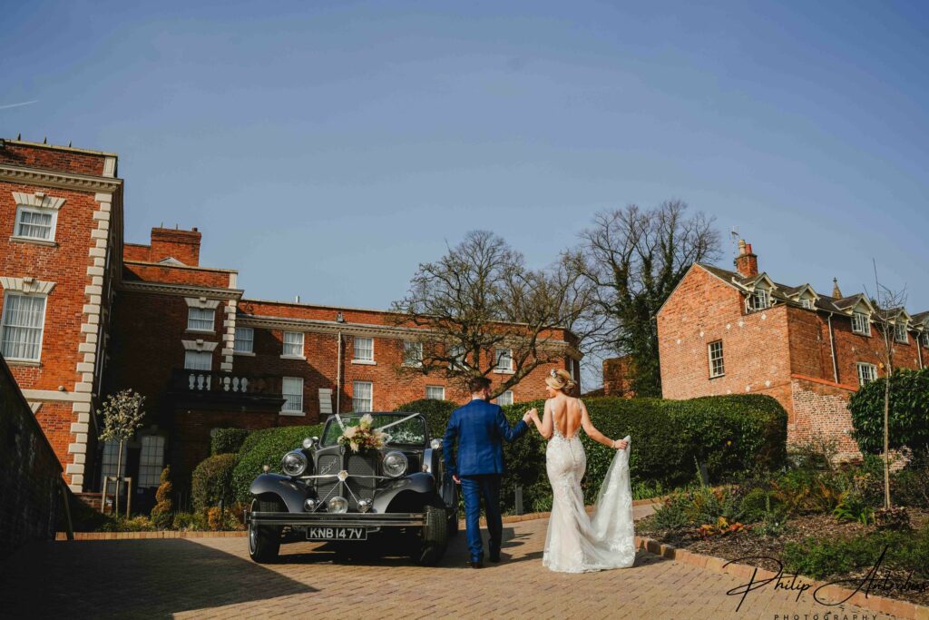 Bride, groom and vintage car at wedding venue.