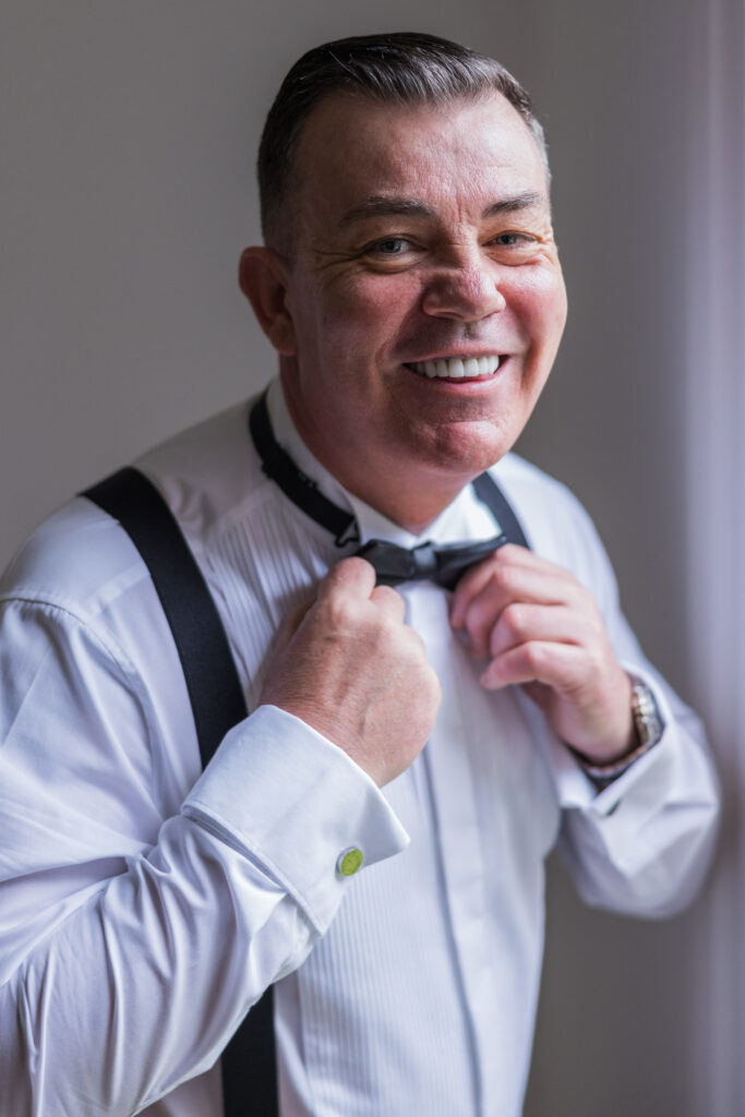 Man smiling while adjusting bow tie.