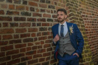 Man in stylish suit posing by brick wall.