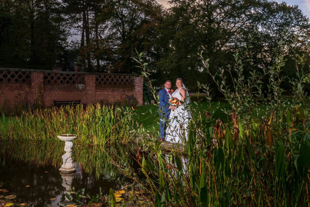 Bride and groom beside pond at twilight.