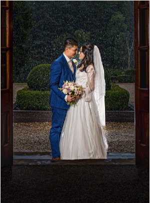 Wedding couple embracing in rain, doorframe view.