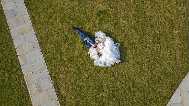 Bride and groom lying on grass, aerial view.