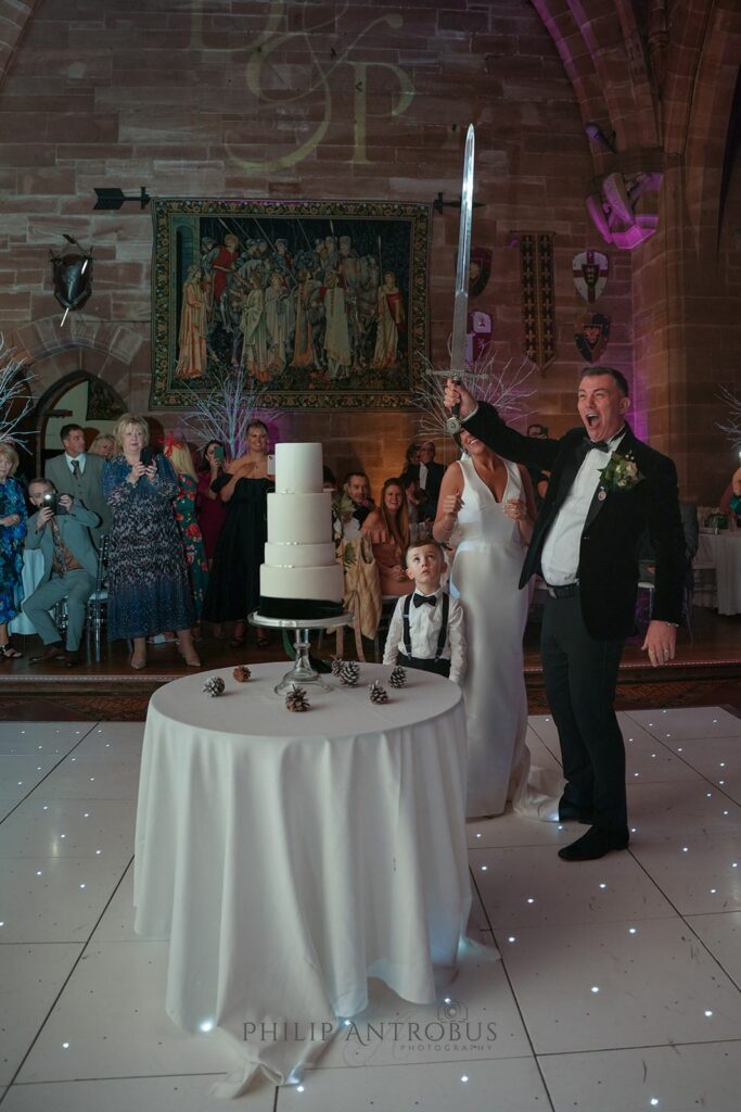 Wedding cake cutting with sword, surprised guests.