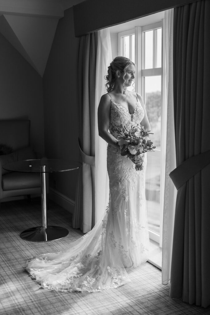 Bride by window at Carden Park  in wedding dress.