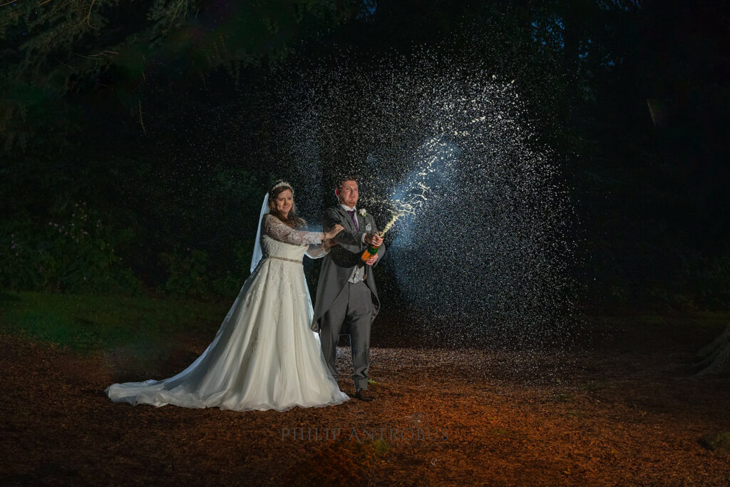 Bride and groom popping champagne at night outdoors at Chester Zoo wedding.