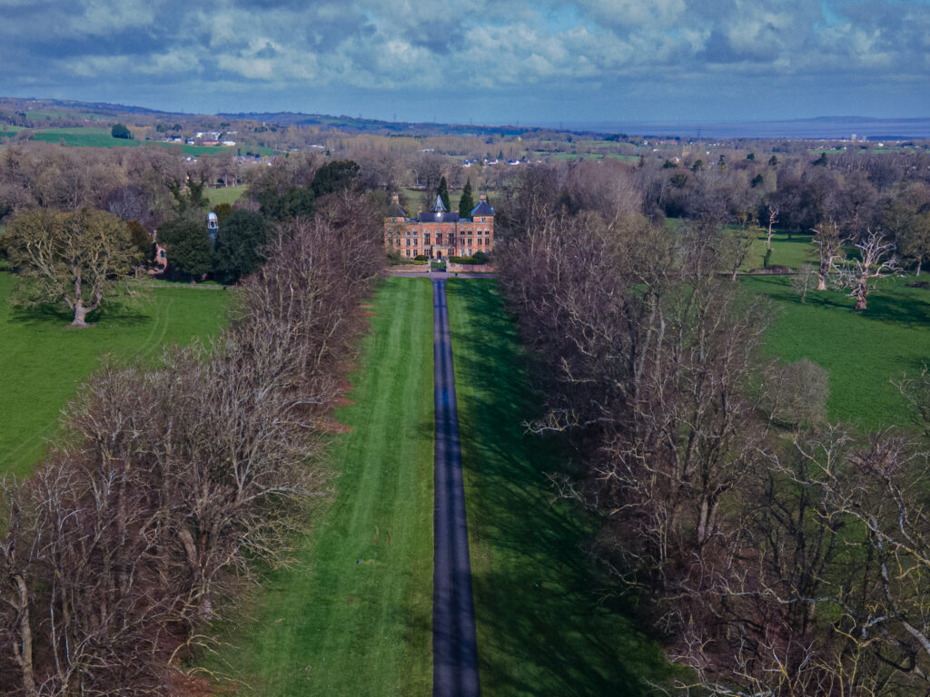 Aerial view of Soughton Hall estate with long driveway and trees.
