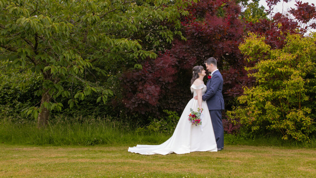 Bride and groom embrace in garden setting.