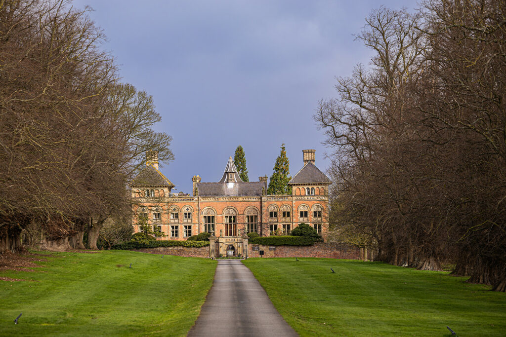 Historic mansion with long driveway and trees.