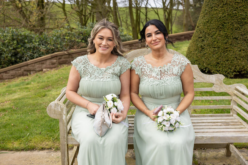 Two bridesmaids sitting on a garden bench at Delamere Manor.