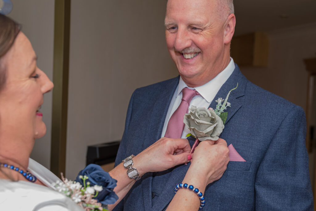 Woman fixing rose on man's suit at wedding.