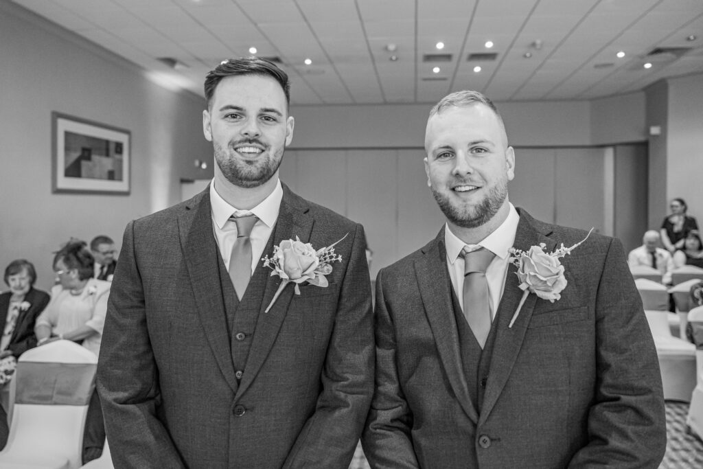 Two groomsmen in suits with boutonnières, wedding setting.