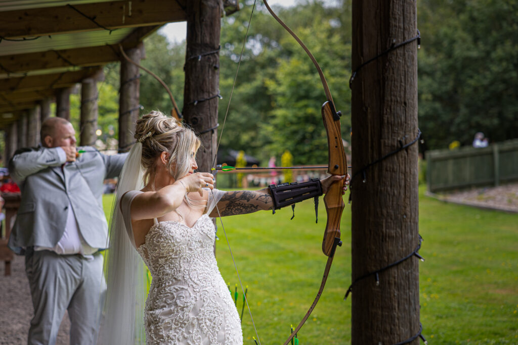 Bride and groom shooting arrows outdoors.