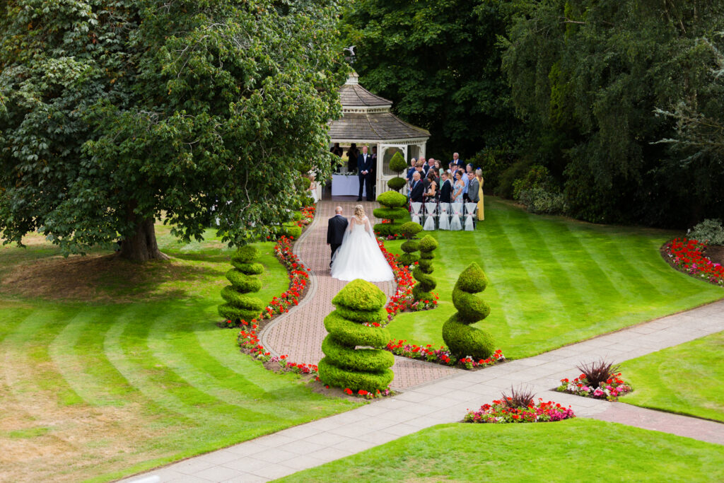 Bride and dad walking garden path to wedding ceremony at Thornton Hall