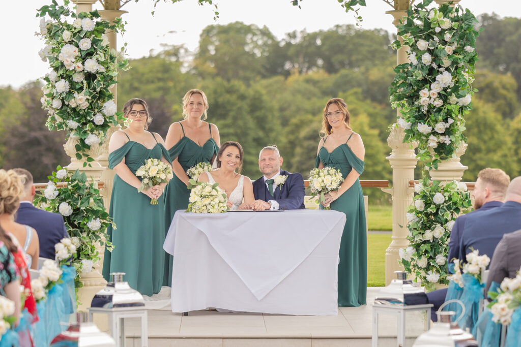 Bride, groom, bridesmaids at outdoor wedding ceremony table at Carden Park Chester