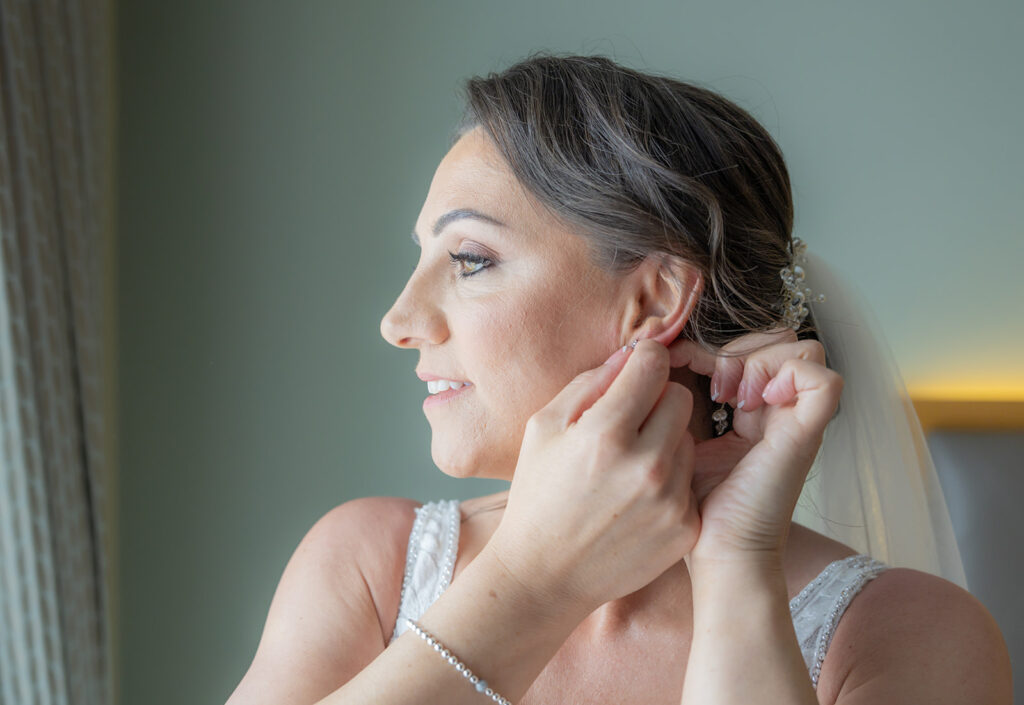 Bride adjusts earring before wedding ceremony. at Carden Park.