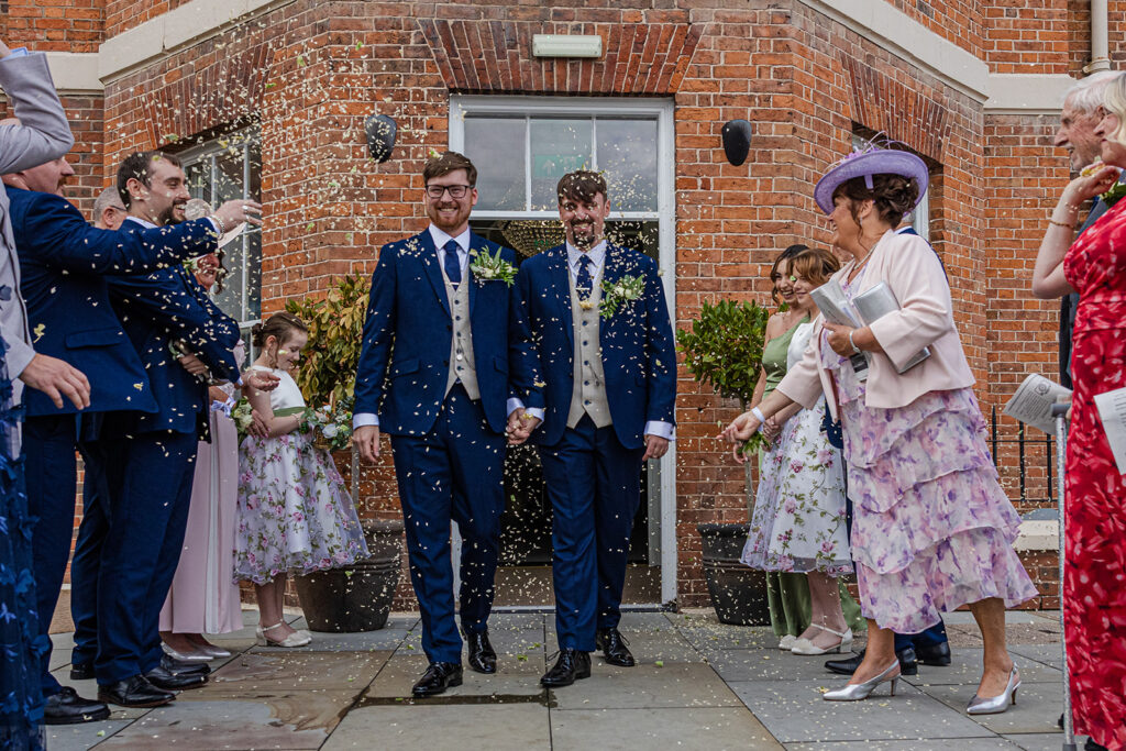 Grooms exiting ceremony amidst celebratory confetti and guests.Chester wedding.