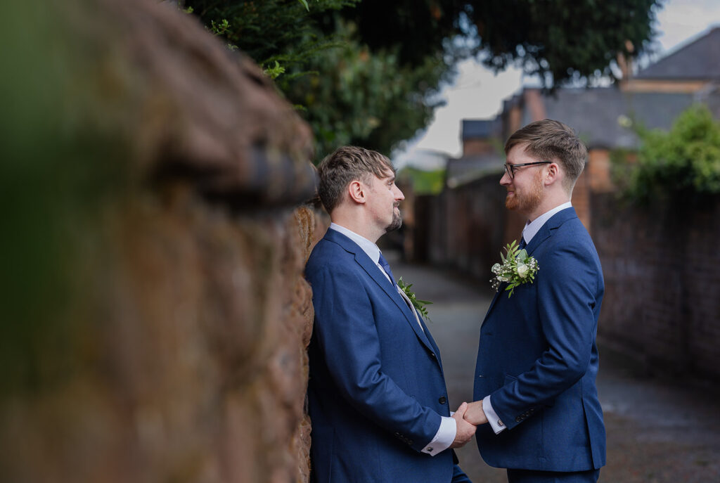 Couple holding hands in the street, wearing suits by The River Dee Chester