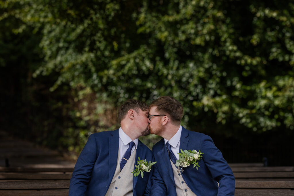 Two grooms kissing in a garden setting.