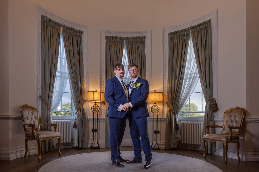 Couple posing in formal attire by large windows.