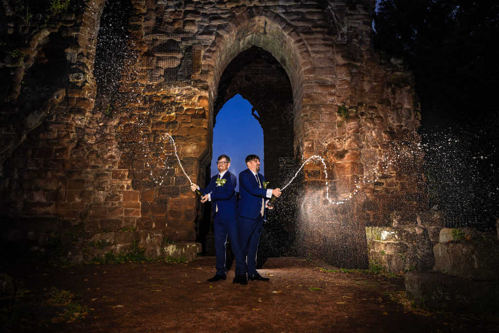 Two men celebrate with champagne at ruins at Chester Wedding