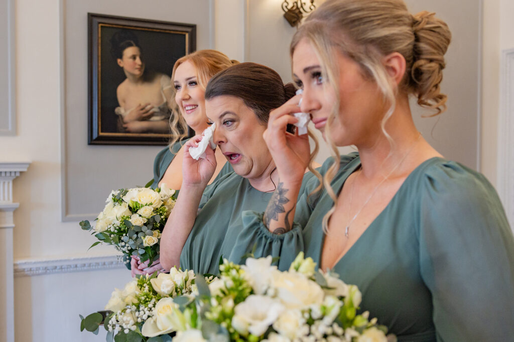 Bridesmaids with green dresses, emotional moment inside room.