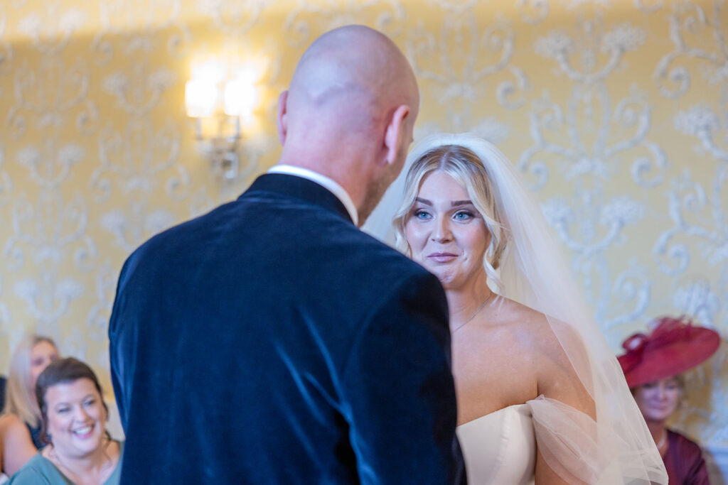 A bride and groom stand facing each other during a wedding ceremony at a charming Chester wedding venue, with guests seated and watching in the background.