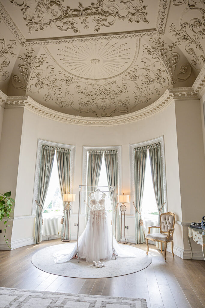 Elegant gown in ornate room with tall windows.
