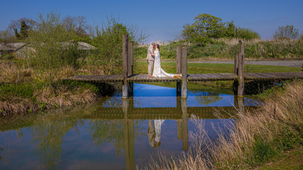 Wedding couple on bridge over pond, sunny day.